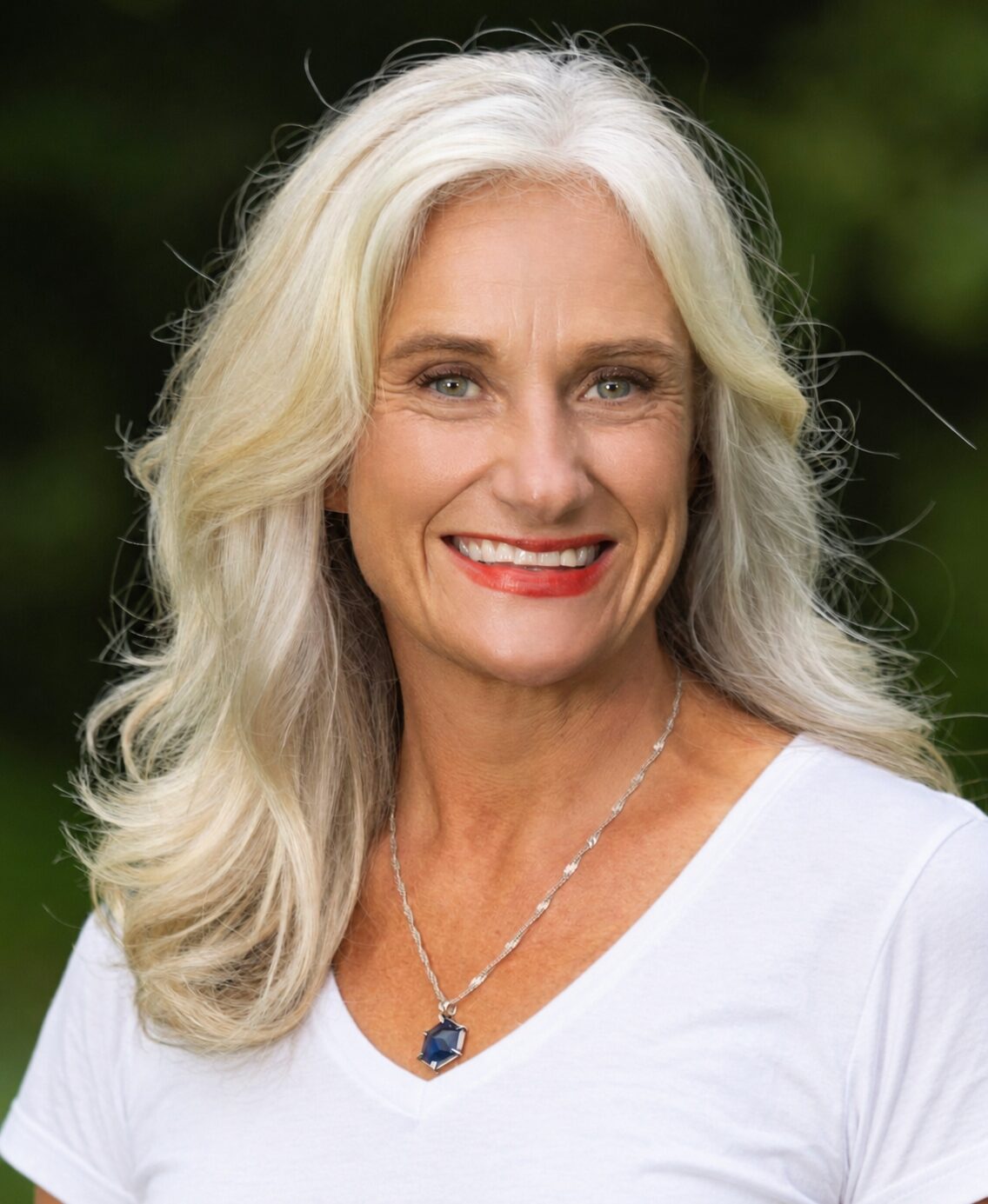Helen Armstrong smiling outdoors, white t-shirt, silver necklace with blue stone.